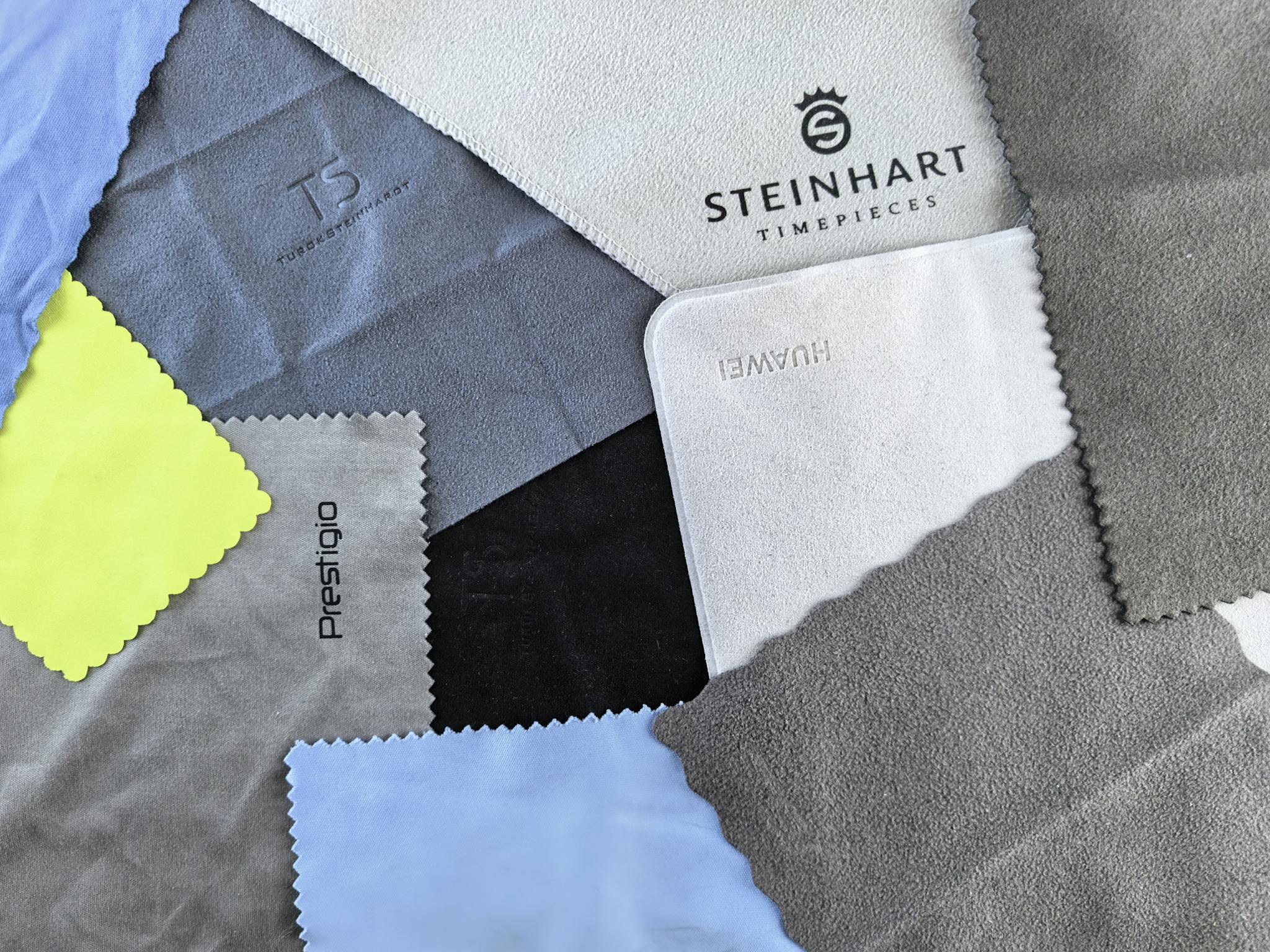 A vibrant flatlay of various cleaning cloths featuring watch brand logos on textured fabrics.
